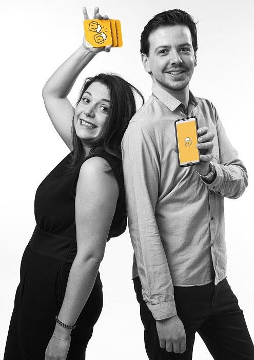 Le fondateur de schlouck map Jules et la co-fondatrice Melissande sont dos à dos en tenant chacun.e.s un téléphone avec dessus l'icône de l'application