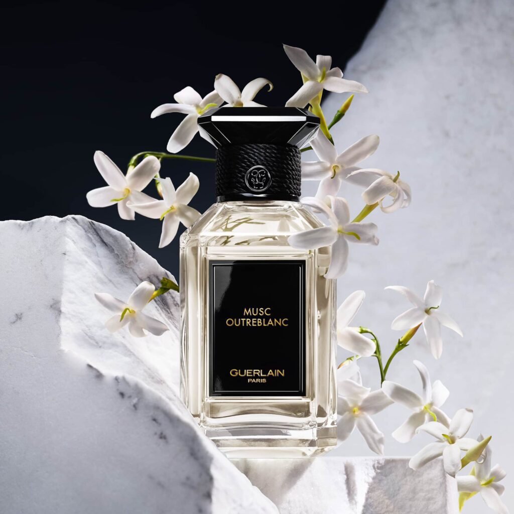Eau de parfum Guerlain Musc Outreblanc avec en fond des fleurs et un arrière fond blanc et noir