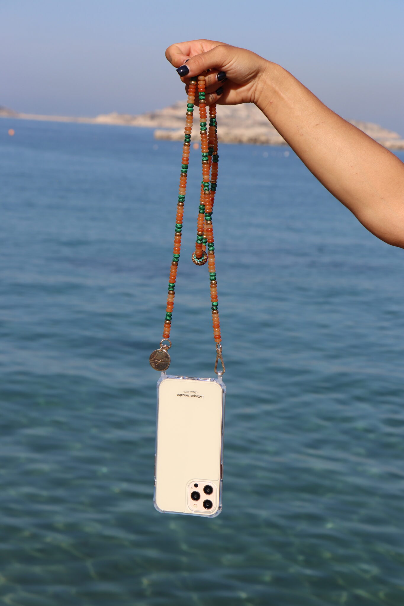 Chaîne de téléphone colorée tenue dans une main face à la mer