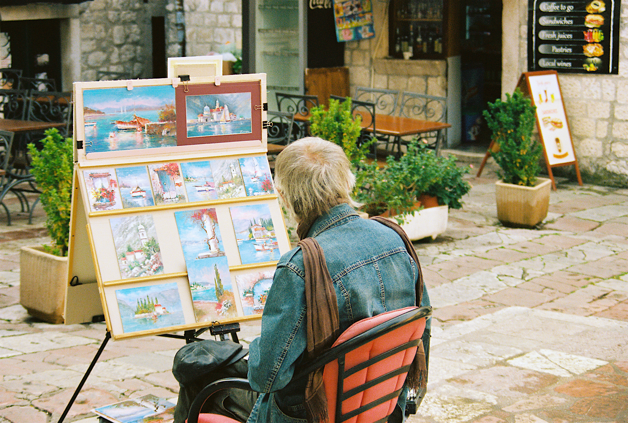 Peintre dans une rue de Kotor avec ses peintures devant lui